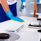 A cleaner sanitizing office desks with professional-grade supplies in a modern office environment.